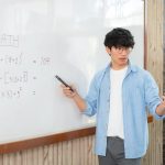 Male tutor standing in front of whiteboard and writing math equation to explaining new lesson